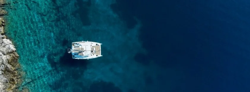 Catamarans anchored in turquoise bay under limestone cliffs at Afales, Ionian Islands.